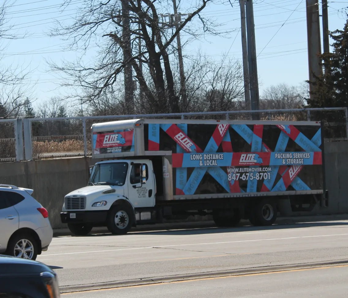 Elite Moving & Storage truck on a road bordered by trees and utility lines in Niles IL